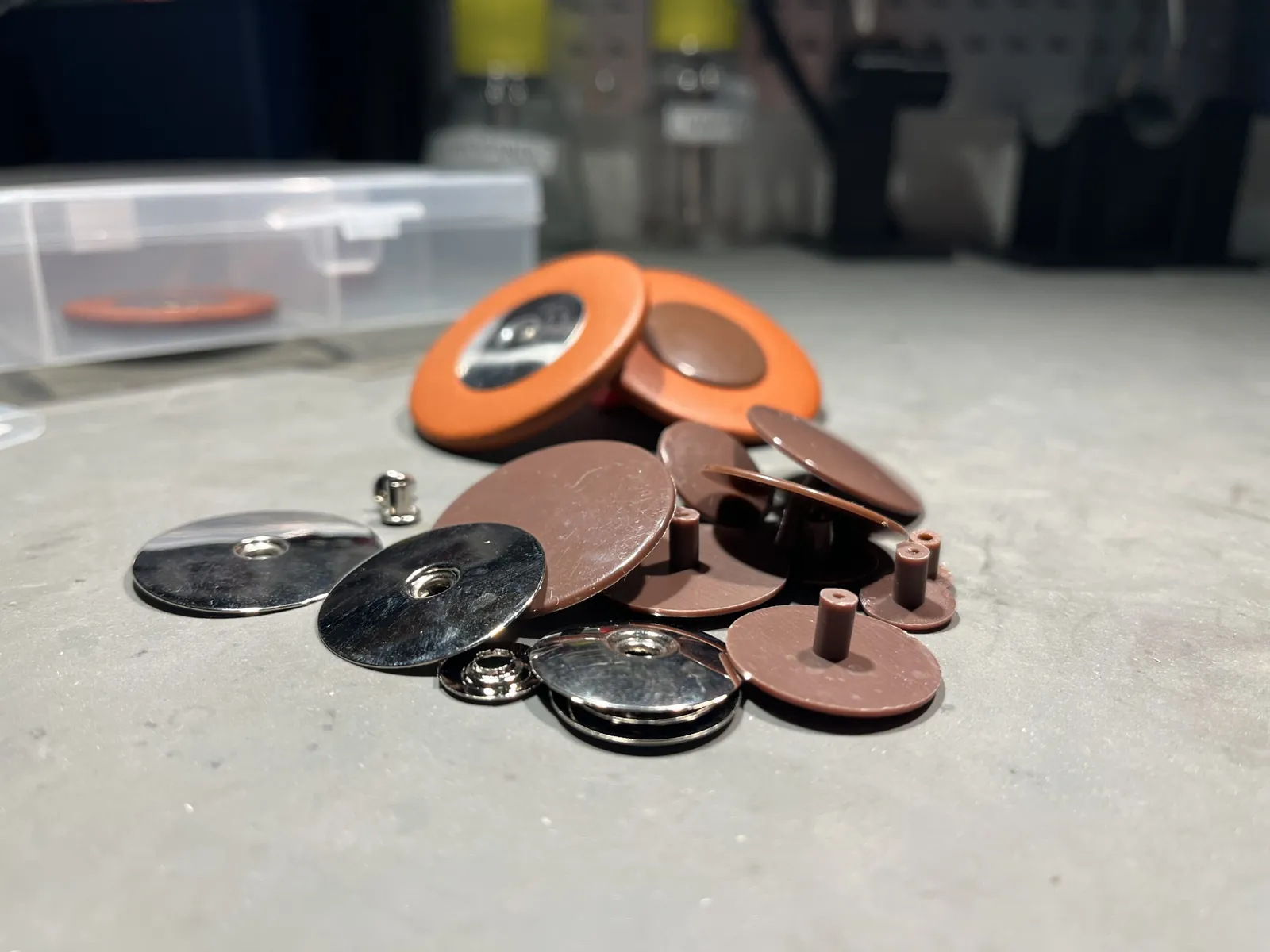 Loose resonators for saxophone pads in shiny metal and brown plastic in front of two large orange pads