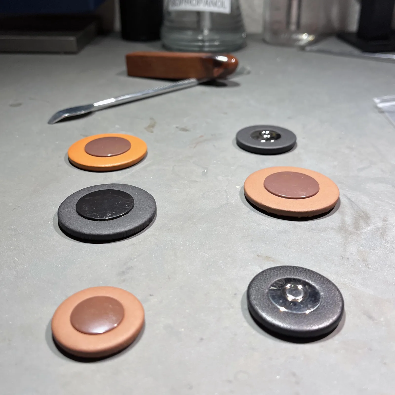 Six different types of saxophone pads in orange, light brown and grey-black leather with plastic and metal resonators on a workbench