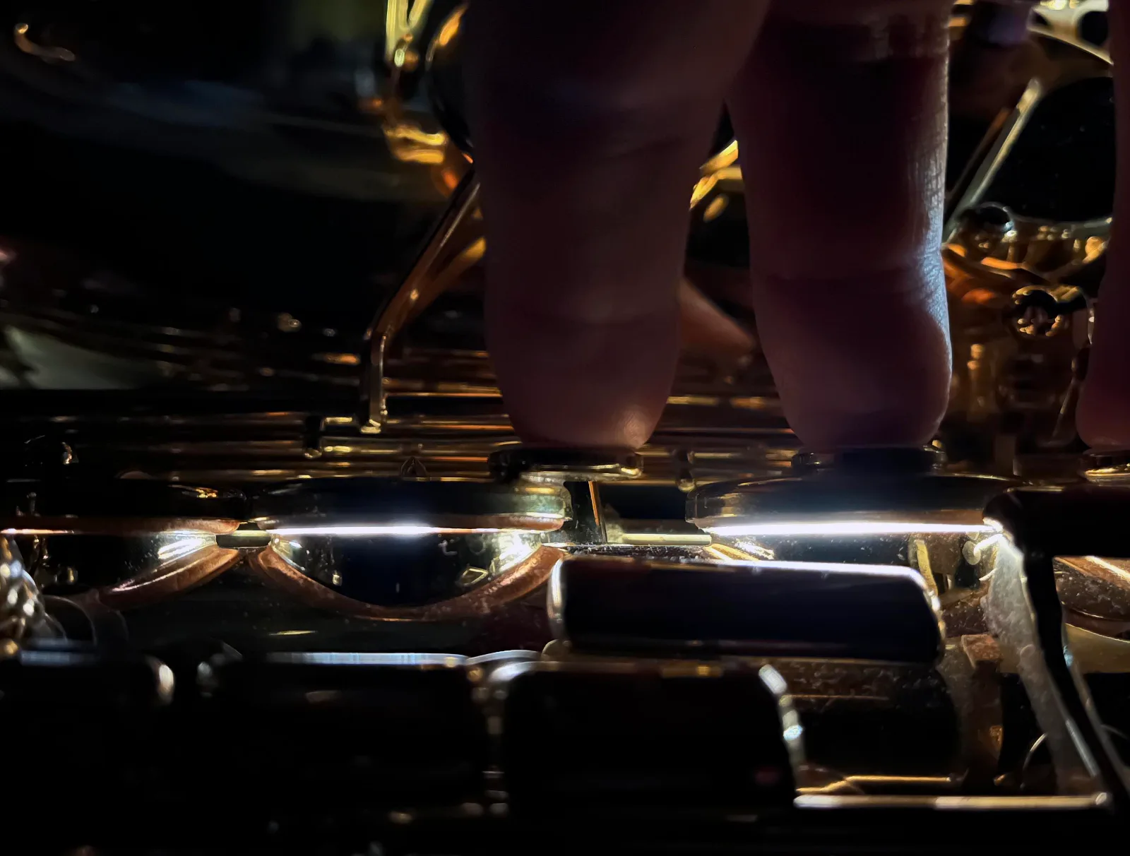 Dark close-up of saxophone keys being pressed down with the fingers while light from a leak light seeps out under the pads