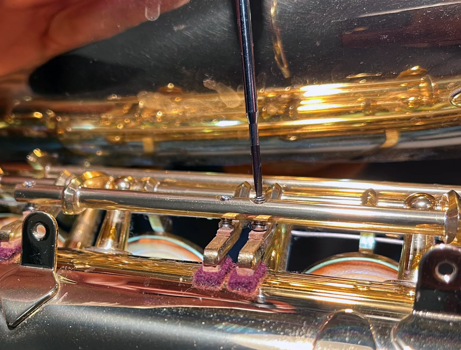 A small screwdriver turning an adjustment screw in the mechanism of a modern saxophone