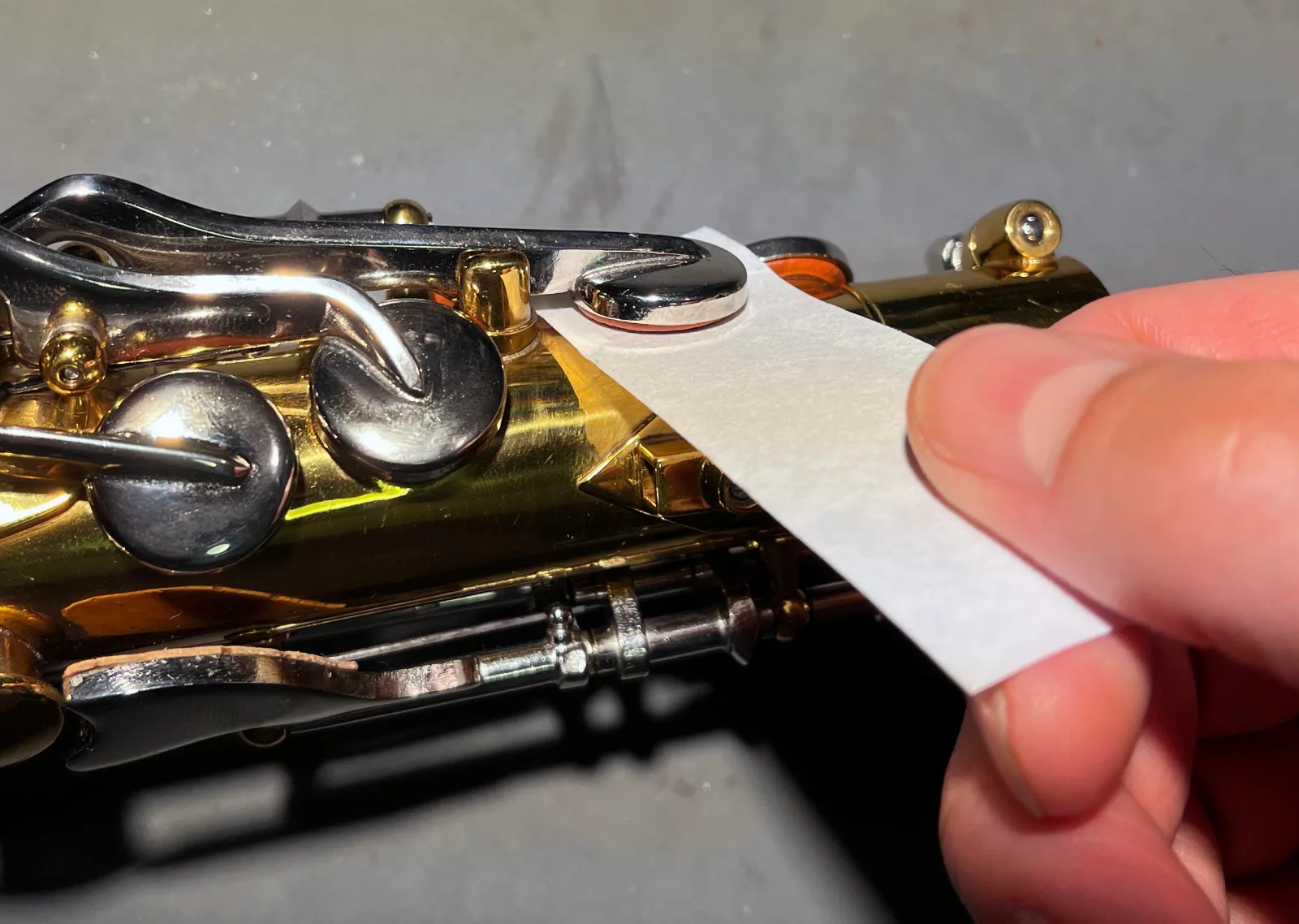Hand holding a piece of cleaning paper placed between the pad and the tone hole under a saxophone key