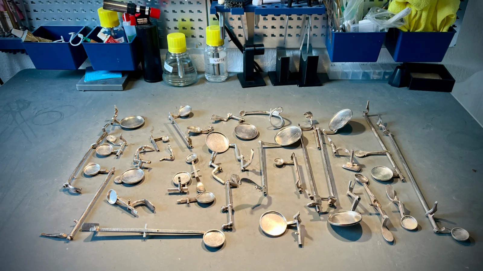 All the keys from a disassembled saxophone laid out on a workbench, with the pad cups emptied of pads