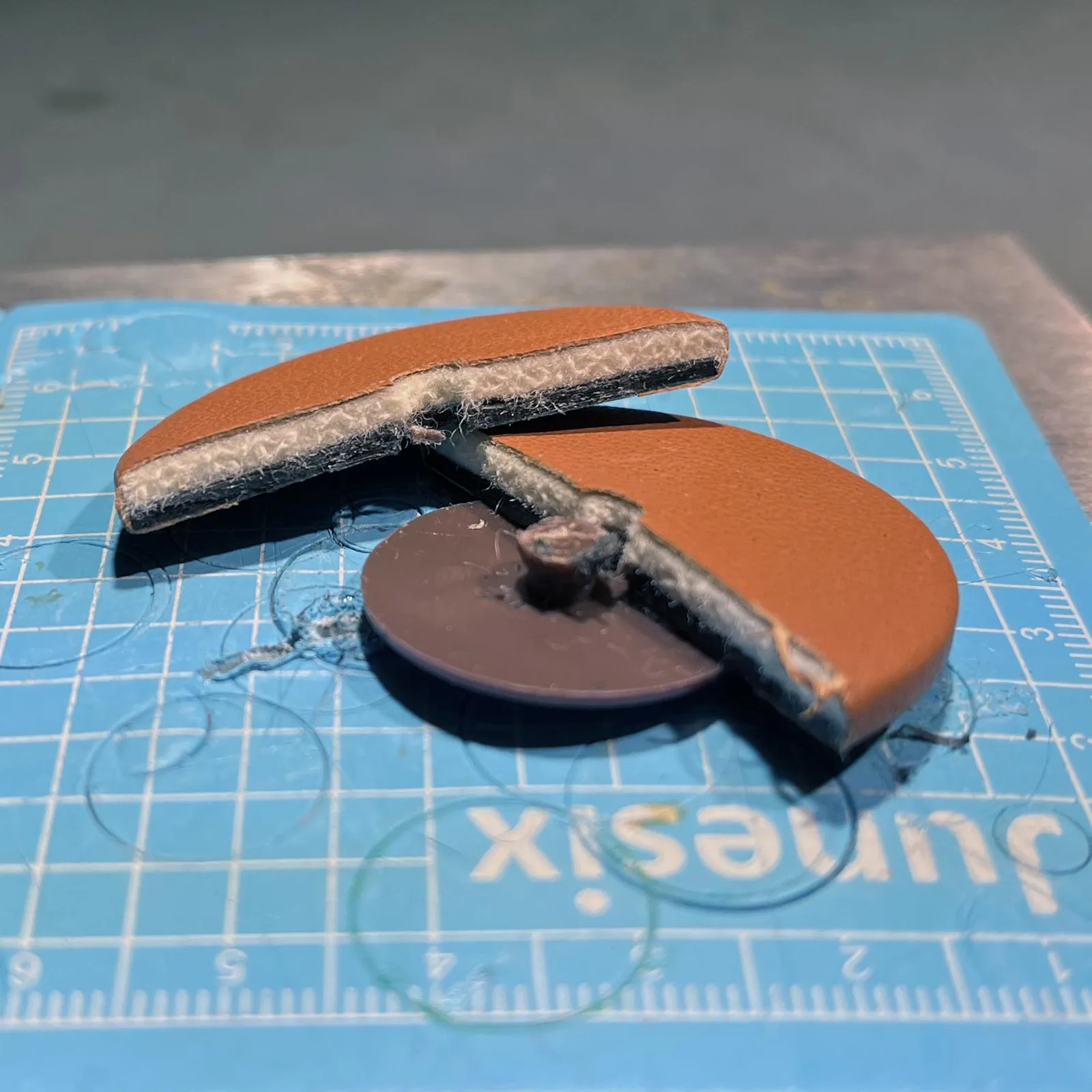 A saxophone pad cut in half, showing the felt core, the leather covering and the backing with resonator