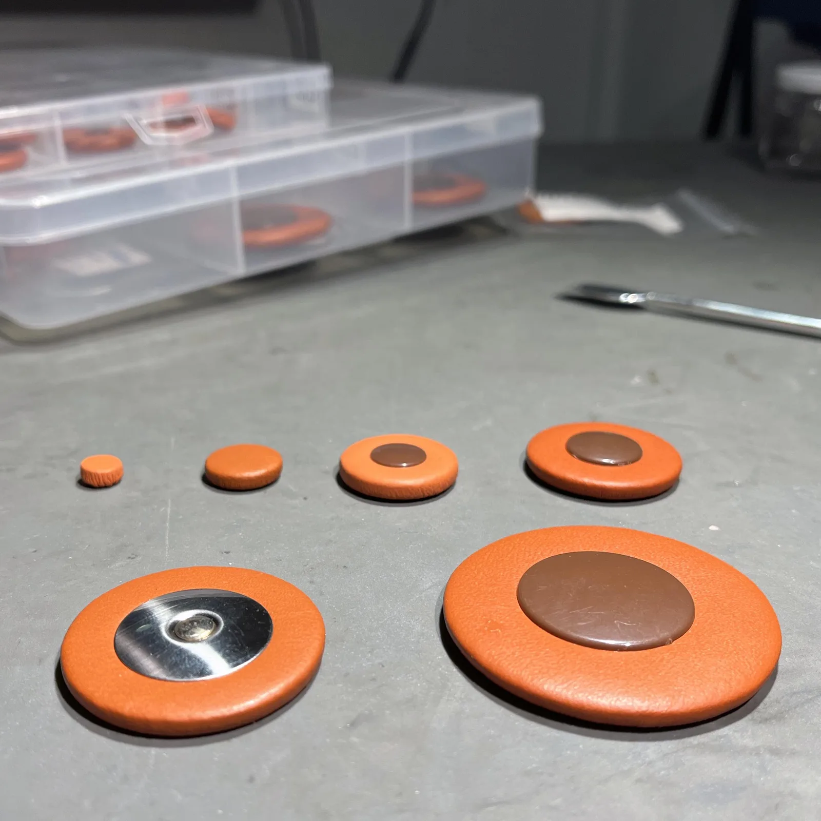 Six saxophone pads of different sizes on the workbench – from a small pad of a few millimetres to a large pad with a resonator