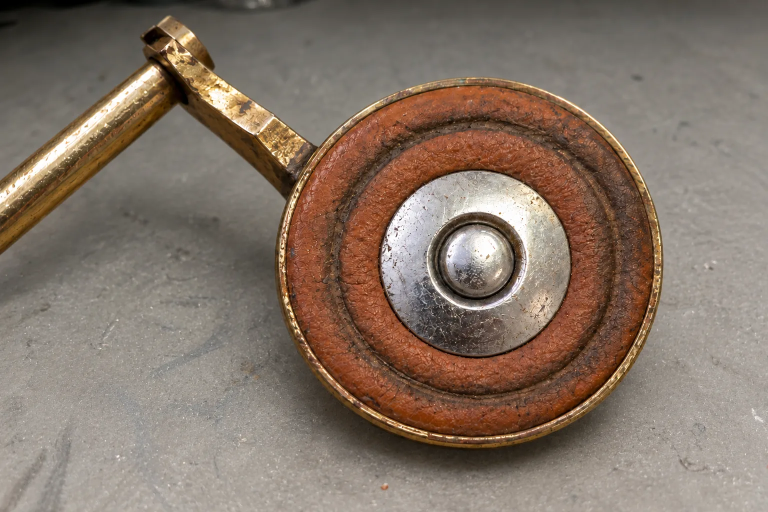 Old saxophone key with a worn pad with a deep impression from the tone hole and dark, hard leather around the metal resonator