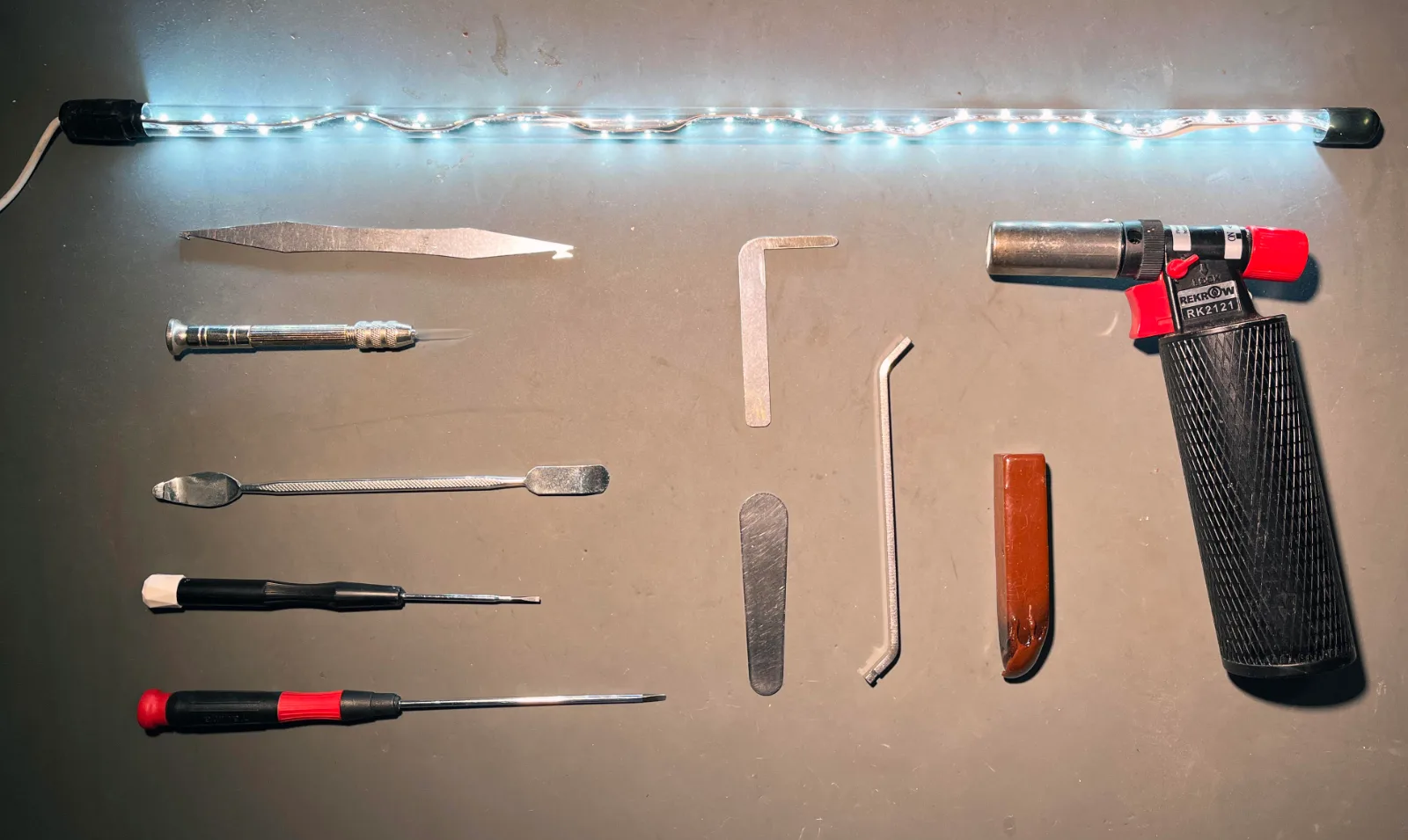 Saxophone tools laid out on a workbench: leak light, screwdrivers, spring hook, feeler, pad iron, shellac stick and gas torch